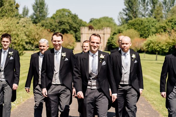 Groom and groomsmen walking towards camera wearing floral buttonholes